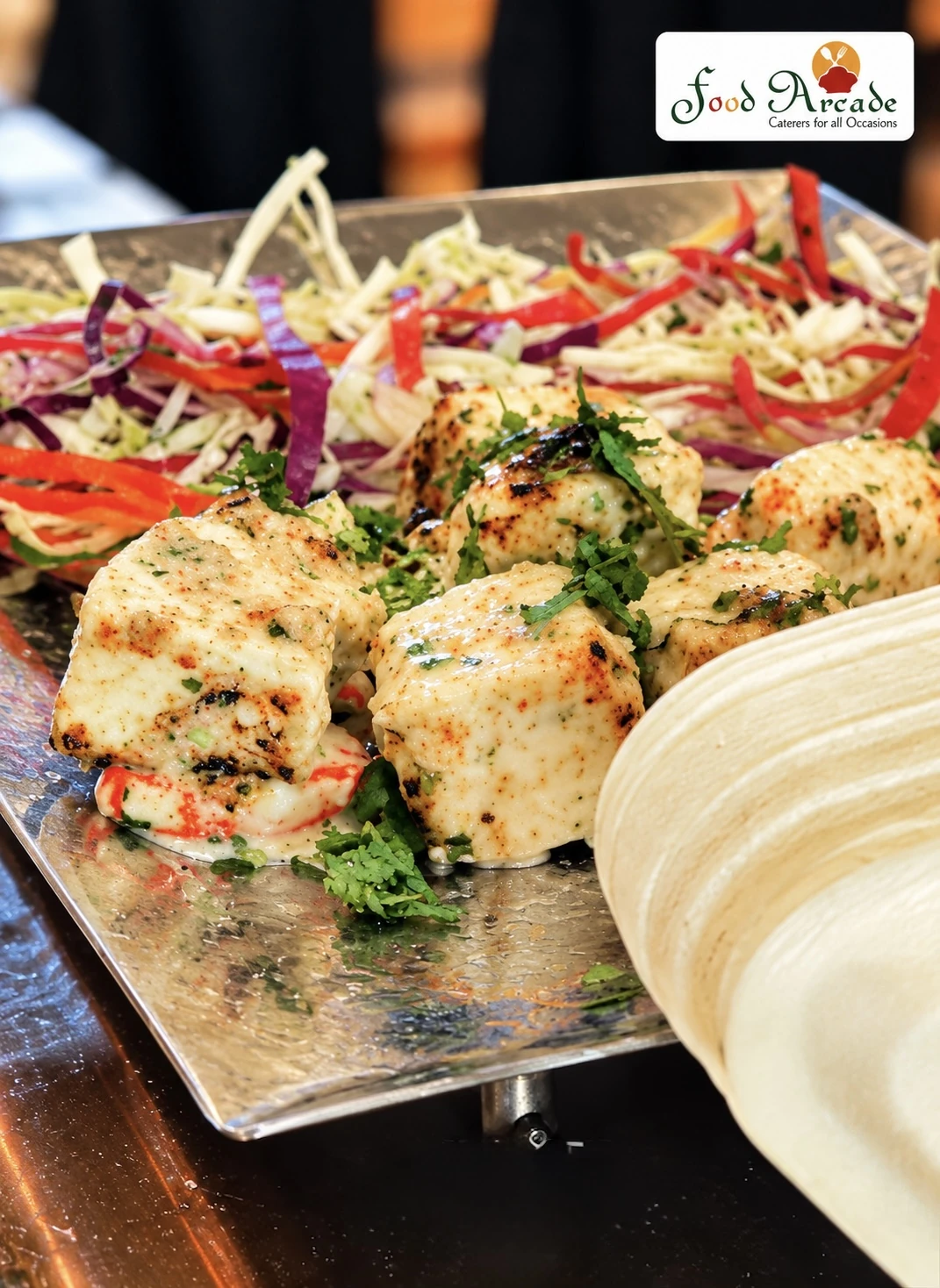 Grilled paneer pieces with herbs on a hammered steel tray with colourful slaw