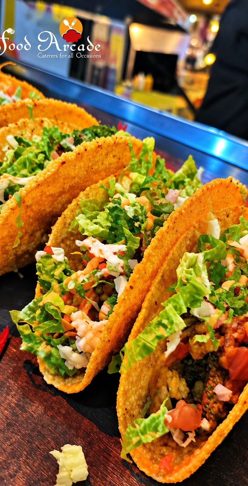 Crisp taco shells filled with lettuce, vegetables and sauces on a wooden board